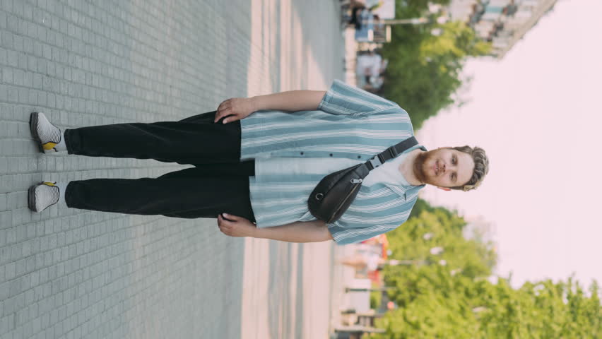 Vertical format time lapse portrait of guy standing in city center while people men and women rushing around. Youth and metropolis concept.