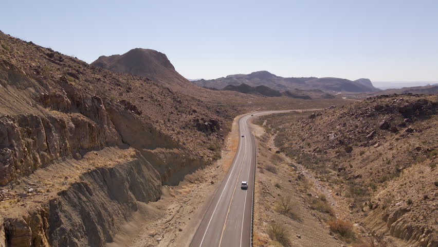 Aerial tracking follows car driving through desert wall and open road in Big Bend National Park Texas