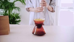 Crop video of a woman putting fine coffee grounds on a paper filter before making pour-over on ground coffee over the paper filter on a glass dripper. An alternative method is called Dripping.
