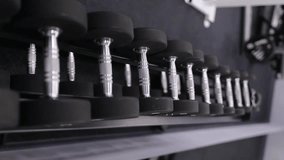 Dumbbells on the rack in the gym. Rack with dumbbells in the gym. Metal dumbbells on the rack for athletic and healthy people for training in the fitness room, vertical orientation video. Dumbbells