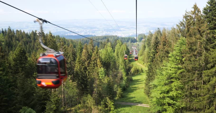 Funicular or cable car ride in the Swiss Alps. Green forest and pines trees, sunny day, red calbe cars, real time, no people