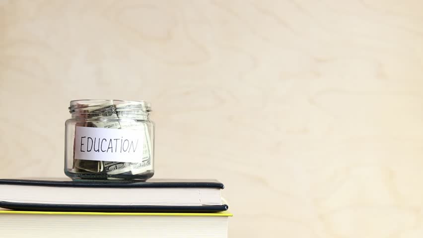 Piggy bank with dollars for education. Accumulation of financial concept. A glass jar with money stands on a stack of books. The woman puts more money in the piggy bank Royalty-Free Stock Footage #1104800629
