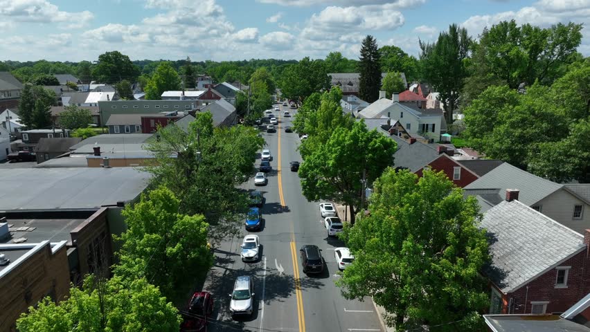 Dolly forward over small town America street during summer. Traffic on road outside of town houses. Aerial shot.
