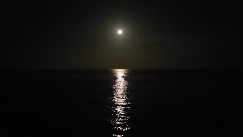 Flying over the ocean waves at night towards the bright moonlit sky. Night scene.