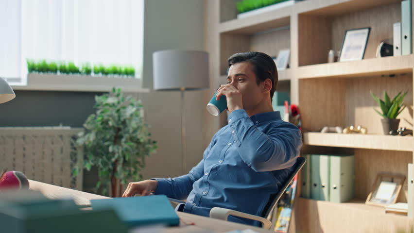 Relaxed startuper drinking coffee working in office closeup. Focused man taking on eyeglasses looking screen indoors. Hardworking businessman staring computer monitor after break at modern workplace | Shutterstock HD Video #1104814359