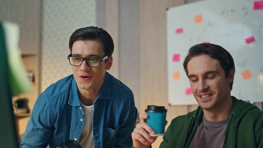 Excited creators discussing computer project at office. Closeup eyeglasses man gesturing hands talking to partner. Smiling emotional freelancer drinking coffee looking at colleague. Designer in work | Shutterstock HD Video #1104814451