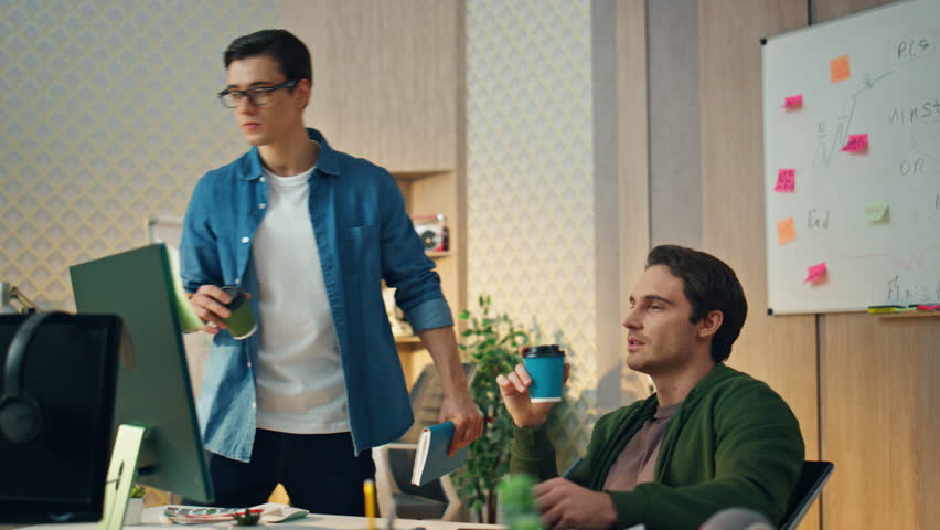 Two creators discussing project at sunny office. Eyeglasses smart man saying opinion going to break. Focused freelancer drinking coffee looking computer screen attentively. Designer involved in work | Shutterstock HD Video #1104814497
