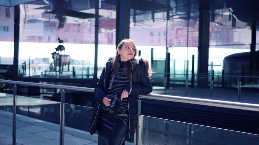 Young Latin woman tourist in warn clothes looking out with professional photo camera in Reina Sofia museum in Madrid, Spain during daytime