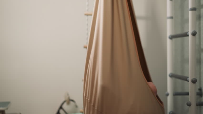 Happy little boy sits in turning hammock chair in home sports gym slow motion. Toddler kid swings in comfortable hanging textile cocoon in playing room