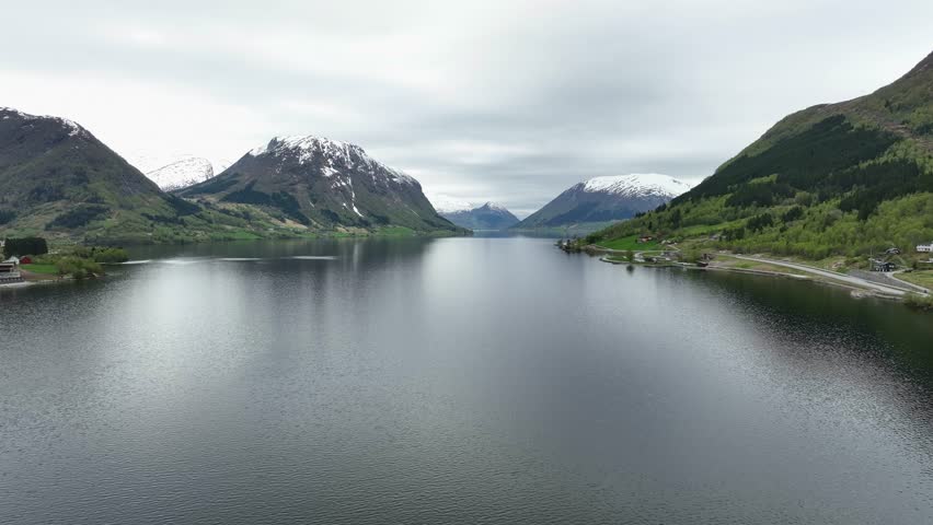 Stunning scenery at Jolstravatn Norway seen from town of Skei - Backward moving aerial above Jolstravatnet lake during early spring morning with green forest and snow capped mountains