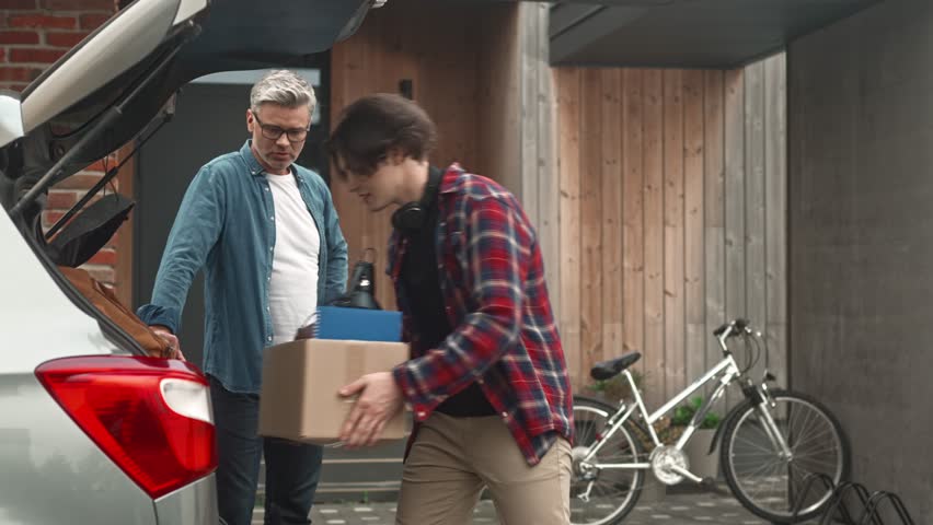 Boy moving out of parent's home. Father helping teenage pack for college. Young guy entering university. Male family members shaking hands and hugging. Relationship between adolescent son and dad.