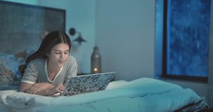 Beautiful Indian woman lying on bed use laptop pleasant talking on video chat with friends late night. Happy excited smiling girl looking computer webcam screen enjoy overtime online work from home