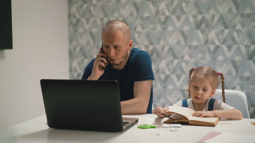 young daughter do homework, sits at table with book, on distance learning, dad sits next, works at computer and talks on phone, say girl not to interfere and not to distract Royalty-Free Stock Footage #1104833397