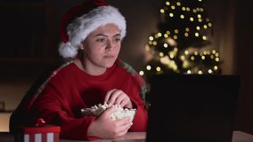 Young woman with popcorn watching movie use laptop at home on Christmas eve