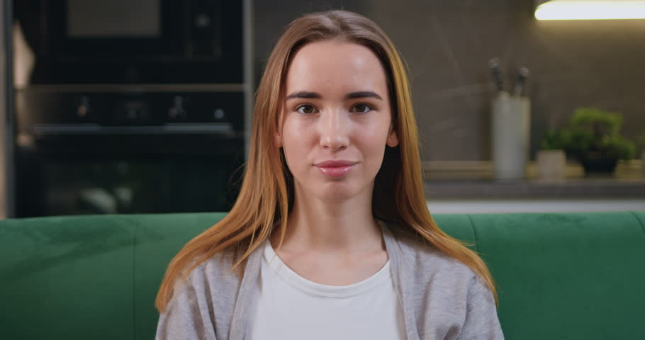 Portrait shot beautiful caucasian teenage girl sitting on green sofa in home kitchen smile look at camera, having wide toothy charming smile, poses indoors