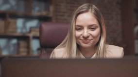 Beautiful cheerful woman watching funny videos on wireless computer during short break at work and smiling. Blonde lady relaxing and having rest after hard working day in company.