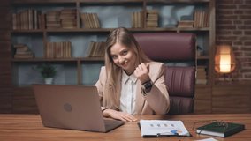 Positive employee inviting colleague to join online video conference on laptop. Cheery female sitting on comfortable office chair and demonstrating welcoming gesture with hand.