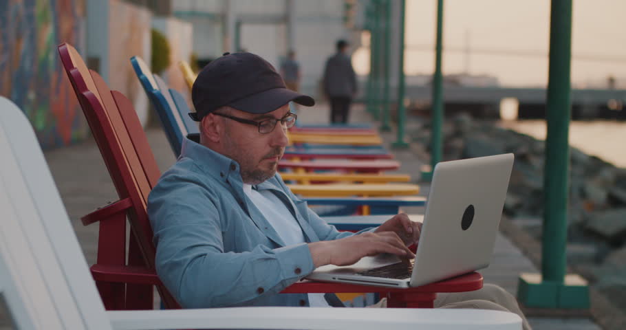 Caucasian Man Using Laptop Outdoors Working Remotely, Ocean Shore in the City. Young Guy Working Remotely at a Computer on the Street. Remote Work, Business. | Shutterstock HD Video #1104846717