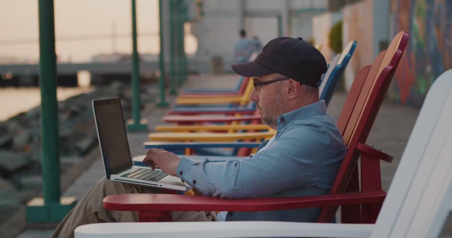 Caucasian Man Using Laptop Outdoors Working Remotely, Ocean Shore in the City. Young Guy Working Remotely at a Computer on the Street. Remote Work, Business. | Shutterstock HD Video #1104846721