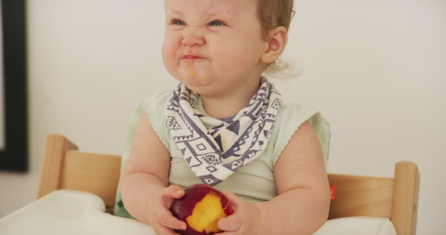 Baby, fruit and healthy eating at home for breakfast with sour and funny face from peach. Young child, food and nutrition of a kid in a high chair feeling hungry and tasting fruits in a house