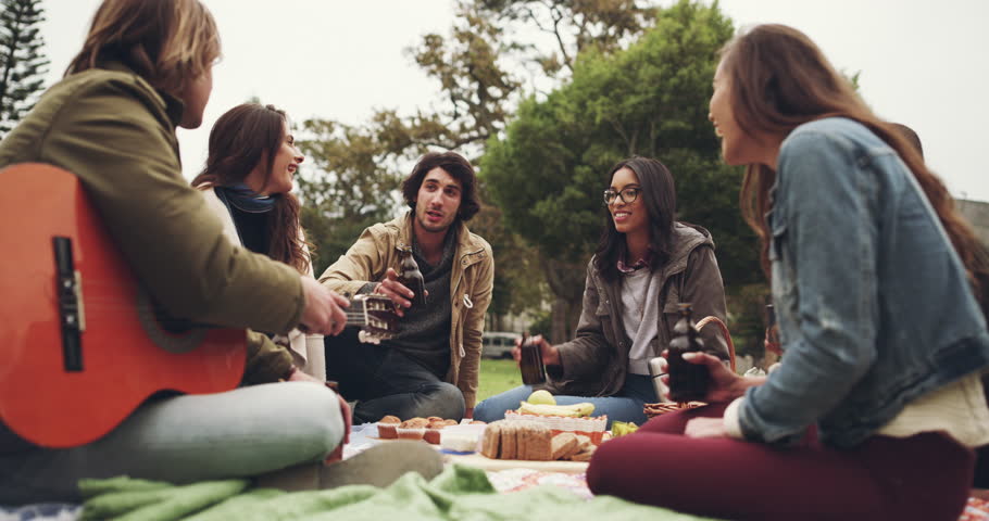 Picnic, cheers and friends celebrate on grass with drinks on holiday, vacation and weekend together. Relax, celebration and happy students with guitar for bonding, fun and happiness with alcohol