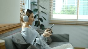 Side view of joyful young woman wearing headphone playing video game on digital tablet at home