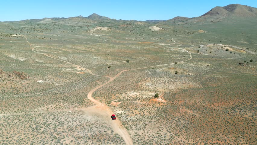 Aerial view of a red truck driving off road thru the Nevada dessert in the Spring with bright greens and colorful sand