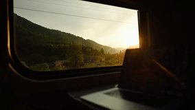 Train compartment, table with a laptop, mountains and sunset outside the window