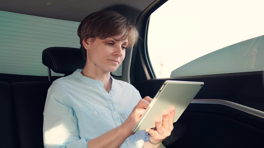 Working with digital tablet. Happy girl goes on journey. Student studies remotely. Online learning on trip. Young student girl is working with tablet computer while sitting in back seat of car | Shutterstock HD Video #1104855731