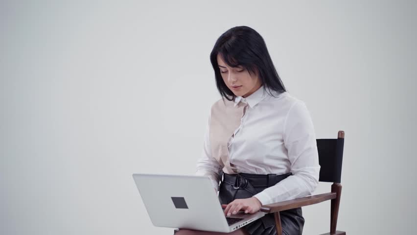 Beautiful woman is typing on a laptop. Attractive girl in white blouse sitting on the chair and printing on a modern gadget. Slow motion.