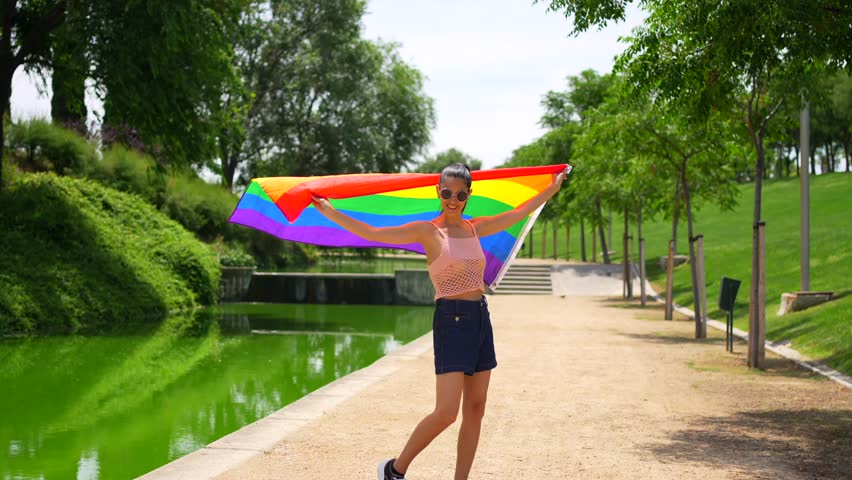 Caucasian brunette woman with a colored flag of LGBT walking through a park, lesbian woman concept
