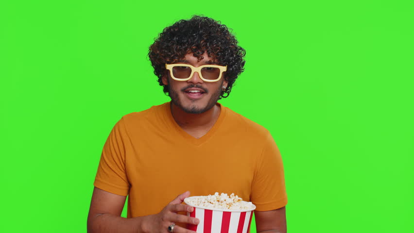 Excited indian man in 3D glasses eating popcorn, watching interesting tv serial, sport game, film, online social media movie content. Hindu guy enjoying domestic entertainment on chroma key background Royalty-Free Stock Footage #1104876759