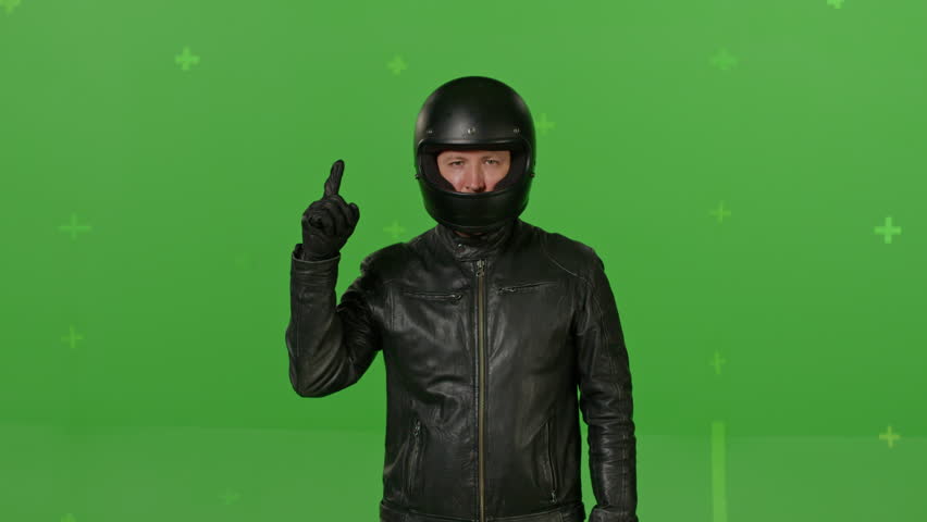 Man with black full Face Motorcycle Helmet standing and pointing with his hands at virtual places on green screen chroma key background. People, modern lifestyle and youth concept.