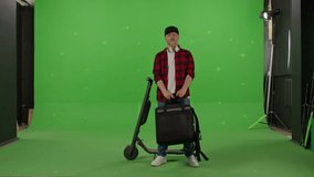 Pizza delivery man listens to music in headphones holds a thermo backpack with food in his hands and looks at the camera on a green background. Copy space on chroma key. 4k slow motion video