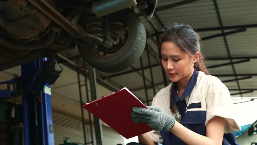 Asian female technician checking car suspension checking brakes left rear wheel bearing carefully and recorded the report on the clipboard for the maintenance of the customer's car at the garage. Royalty-Free Stock Footage #1104880063