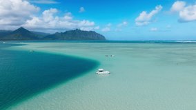Scenic Oahu shore on Hawaiian paradise island. Amazing nature landscape blue lagoon. Aerial view of boat with snorkelers out on the Kaneohe sandbar tour with cinematic Kualoa Mountains on background