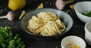 Person sprinkling pasta with parsley, plate with spaghetti on table decorated with herbs, lemon and garlic, 4k footage, high quality horizontal video clip
