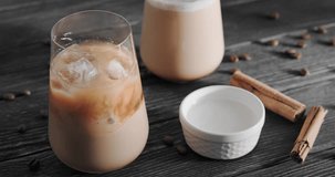 Person grabbing a glass with iced latte drink with milk froth and ice cubes, couple of cool coffee drinks placed on black wooden table, slow motion clip, 4k close up footage, horizontal video