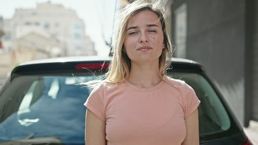 Young blonde woman holding new driver license standing by car at street