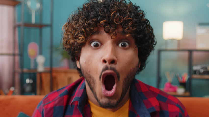Oh my God, Wow. Young indian man surprised looking at camera with big eyes, shocked by sudden victory, good win news, celebrating. Portrait of excited amazed hindu guy at home apartment room on sofa | Shutterstock HD Video #1104894087