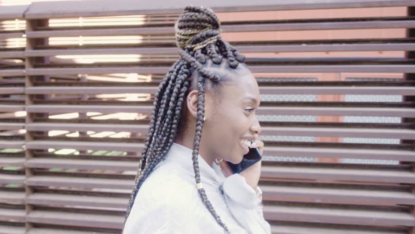 Side view of african business woman with braids talking on mobile phone and walking down the street