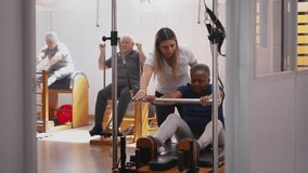 Female Pilates coach assisting a senior black woman in group class. Candid scene of sport instructor owner of wellness business service - Powered by Shutterstock - Get 15% off with code: PIKWIZARD15