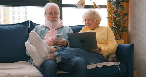 Senior people gadgets in room. Happy elderly couple on sofa in