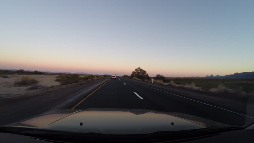 A camera mounted on the dash of a car shows a remote desert road as it passes by a police car.