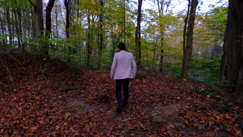 Man running fast through the deserted forest, teenager running away on the path where brown dried leaves are falling