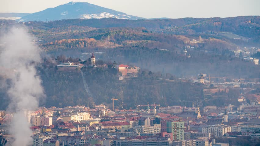 Timelapse of the Schlossberg in Graz while sunrise with chimney smoke in the foreground