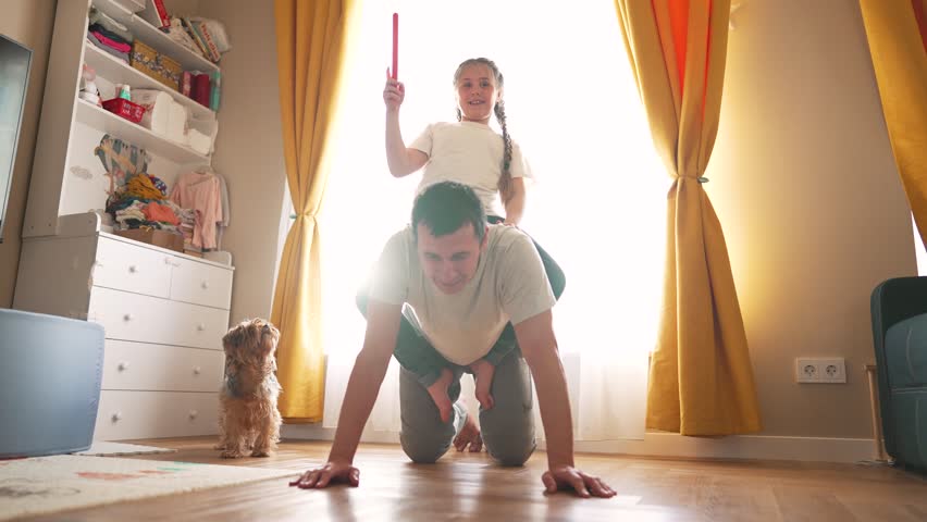 Happy family together, dad, daughter play in house on floor. Dad rolls daughter on back, playing with child. Dad crawling on floor carrying daughter on back, rolling baby on back, having fun together Royalty-Free Stock Footage #1104907559