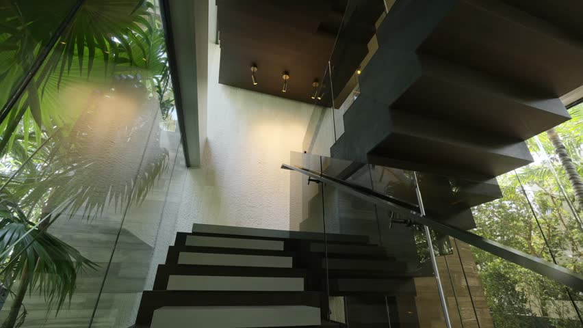 Dark concrete stairs with glass fencing inside luxury modern villa surrounded with green tropical plants. Contemporary interior design elements Royalty-Free Stock Footage #1104908883