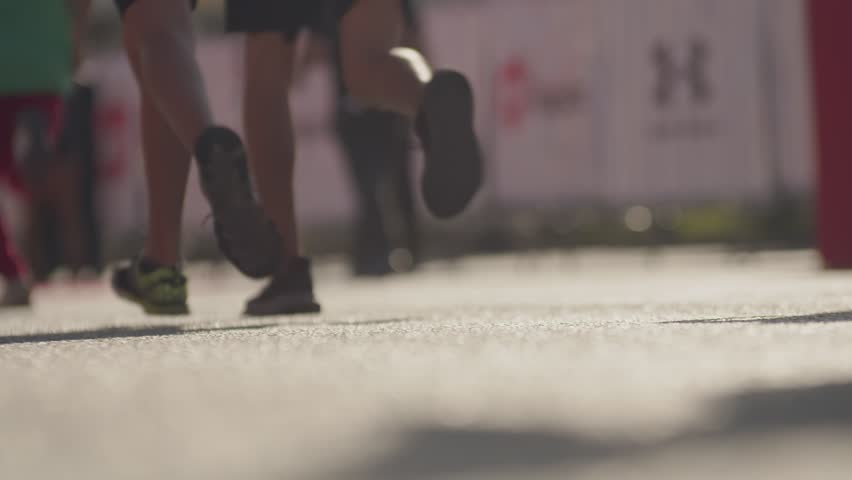 close-up view from the ground in the frame only legs, a crowd of people running on a sunny day. People participate in a race, a marathon in the city