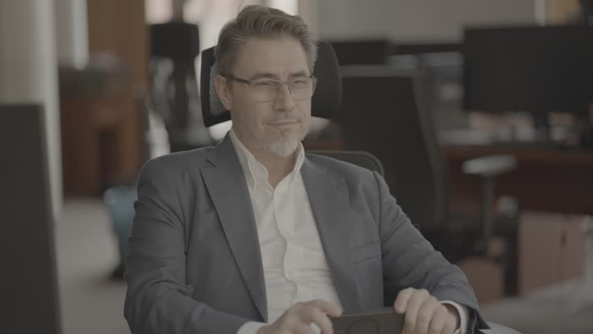 Business portrait - confident businessman sitting at desk working in office, using phone. Happy mid adult man in shirt and jacket, smiling. Video in LOG format - S-LOG3 Cine. Royalty-Free Stock Footage #1104910413